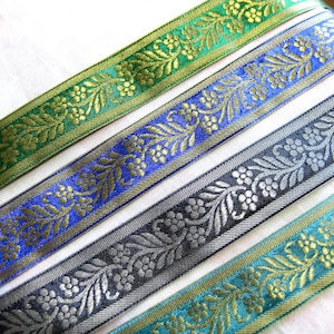 Può includere: Quattro diversi bordi di nastro di broccato dorato e argentato con un motivo floreale. I nastri sono verde, blu, nero e turchese.