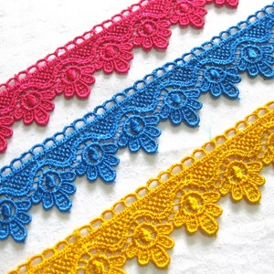 May include: Three pieces of colourful lace trim with a scalloped edge. The lace is a delicate floral design in pink, blue, and yellow.