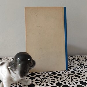 May include: A vintage paperback book with a plain white cover and a blue spine. The book is sitting on a white crocheted doily.