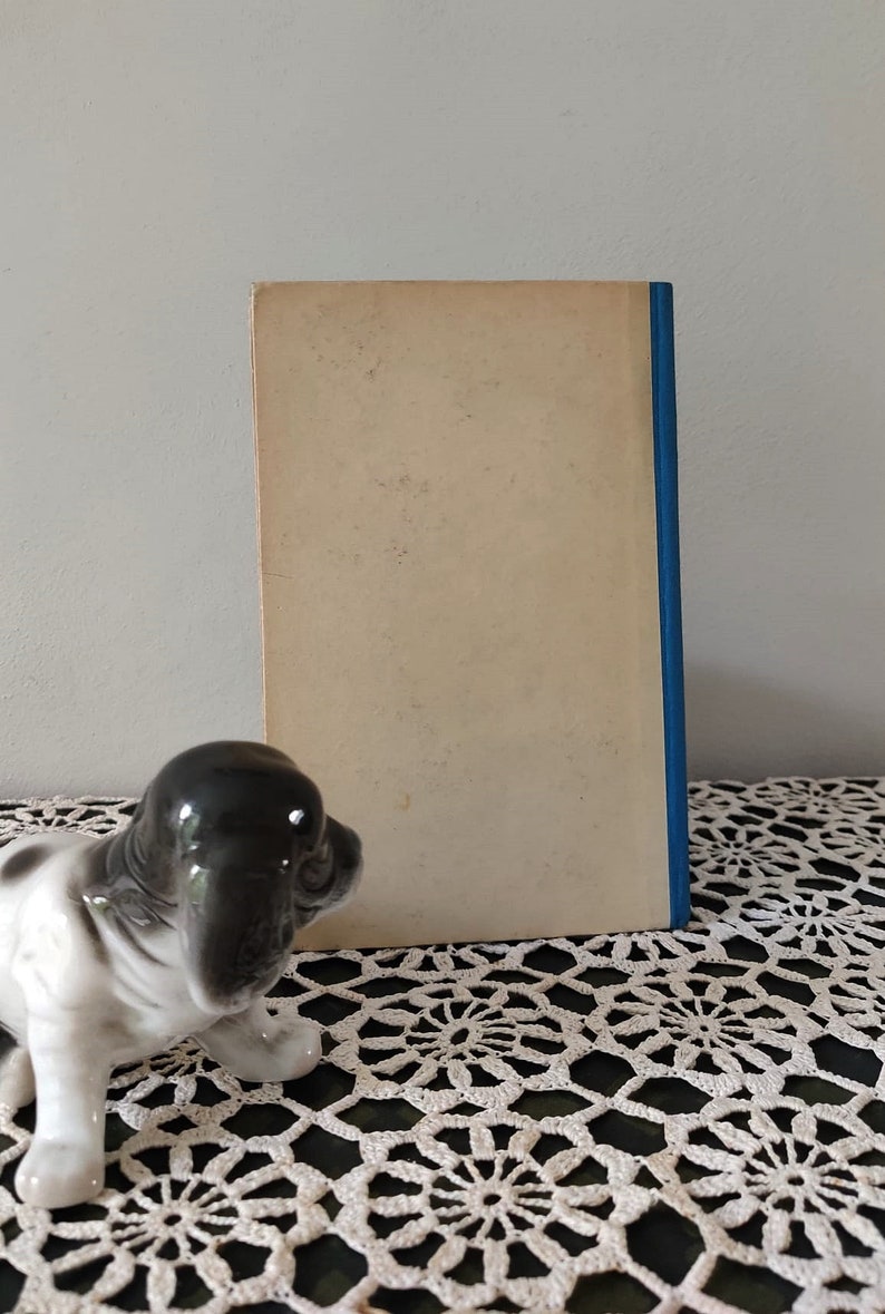 May include: A vintage paperback book with a plain white cover and a blue spine. The book is sitting on a white crocheted doily.
