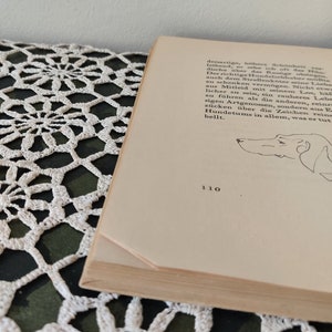 May include: A close-up of a page from a book with a black and white illustration of a dog's head. The text on the page reads "dersartige, h&ouml;here Sch&ouml;nheit leihend, so sehe ich oft das Hon dische &uuml;ber das Ramige obeig Der richtige Hundeliebhaber m&uuml;&szlig;te auch dem Stra&szlig;enk&ouml;ter seine Liebe zu schenken verm&ouml;gen. Nicht etw aus Mitleid mit seinem Los, h&auml;l licher zu sein, ein rauheres Lebe zu f&uuml;hren als die anderen, reinrs sigen Artgenossen, sondern aus E z&uuml;cken &uuml;ber die Zeichen reins Hundetums in allem, was er tut bellt." The page number is 110.