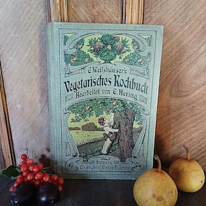 Könnte beinhalten: Ein gebundenes Vintage-Buch mit dem Titel E.Weilshäuser's Vegetarisches Kochbuch, hellgrüner Einband mit einer Illustration einer Person, die Früchte von einem Baum pflückt, dazu zwei gelbe Birnen und eine rote Beerenrispe.