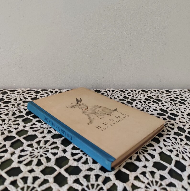 May include: A vintage book titled "Hunde" by B. & P. Dolbin. The book cover features a black and white illustration of a dog. The book is bound in a blue cover with the title "Dolbin's Hunde" printed on the spine.