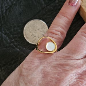 May include: Gold ring with a white oval stone set in a cutout design.