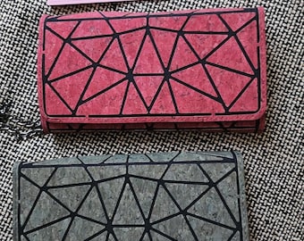 May include: Two rectangular wallets with geometric designs. One wallet is a reddish-pink color, and the other is gray. Both wallets have black geometric patterns. A ruler is placed above the wallets, showing measurements in inches.