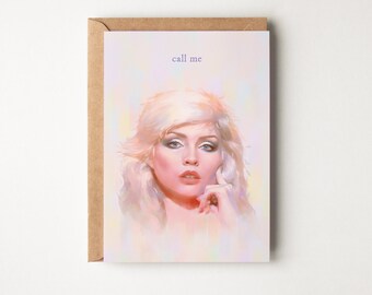 May include: Greeting card featuring a portrait of a woman with blonde hair and blue eye shadow. The text "call me" is printed in a light purple color at the top of the card. The card is inside a brown envelope.