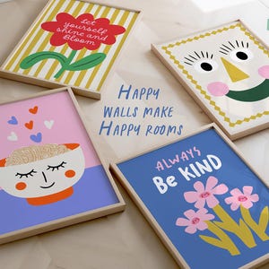 May include: Four framed art prints with cheerful designs. One shows a red flower with the text "Let yourself shine and Bloom." Another has a smiling face. The third has a bowl with a face, and the fourth says "Always Be Kind" with flowers. The text "Happy Walls Make Happy Rooms" is also visible.