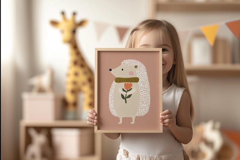 May include: A framed art print featuring a whimsical illustration of a hedgehog holding a flower. The hedgehog has a cream-colored body, a green scarf, and a light brown frame. The background is a soft pink.