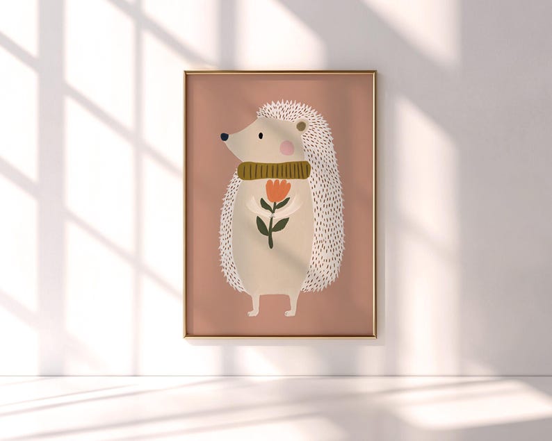 May include: A framed art print featuring a whimsical illustration of a hedgehog. The hedgehog is depicted with a beige body, white quills, and a green scarf, holding a red and orange flower. The background is a muted pink.