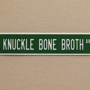 May include: A green street sign with white lettering that reads "KNUCKLE BONE BROTH AVE".