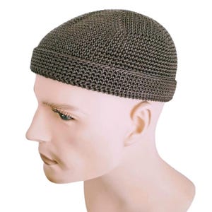 Könnte beinhalten: Eine dunkelbraune Strickmütze. Die Mütze besteht aus einem strukturierten Strickstoff und hat einen umgeschlagenen Rand. Die Mütze wird auf einem Schaufensterkopf präsentiert. Die Mütze ist neutralfarben und kann von jedem getragen werden.