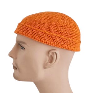 Könnte beinhalten: Eine orangefarbene gehäkelte Beanie-Mütze. Die Mütze hat einen umgeschlagenen Rand und ist einfarbig. Die strukturierte Garnmütze wird auf einem Schaufensterkopf gezeigt.