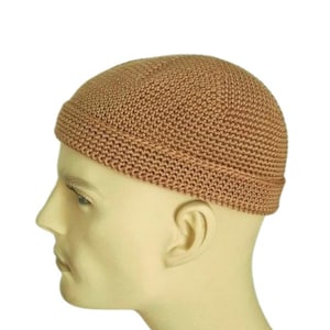 Könnte beinhalten: Eine hellbraune, gestrickte Schädelkappe. Die Kappe besteht aus einem dicht gewebten Material und hat eine abgerundete Krone. Der Rand ist einfach, gefaltet. Die Kappe wird auf einem Schaufensterkopf gezeigt.