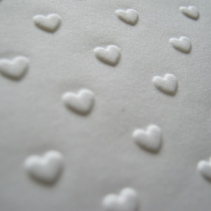 Puede incluir: Tela blanca con un patr&oacute;n repetido de corazones en relieve.