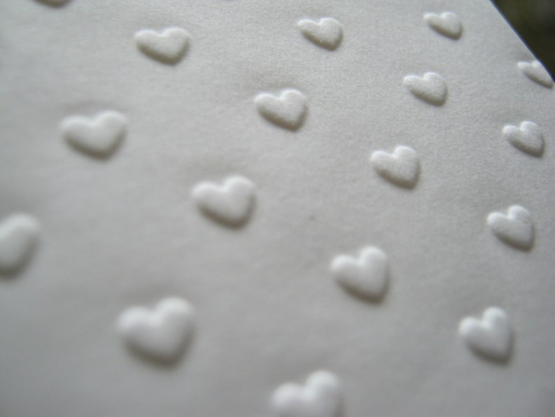 Puede incluir: Tela blanca con un patr&oacute;n repetido de corazones en relieve.