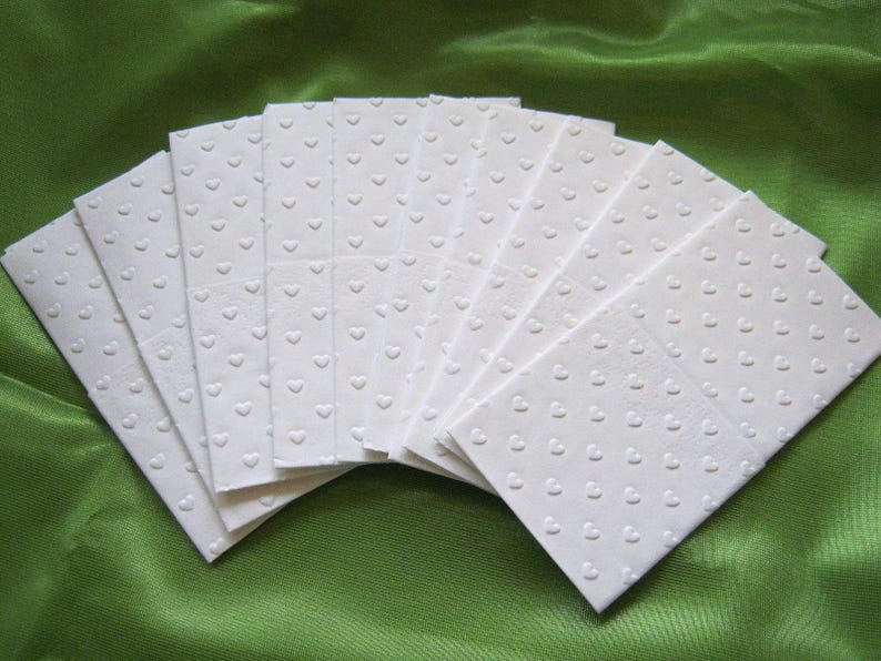 Puede incluir: Una pila de papel de seda blanco con un patr&oacute;n de corazones. El papel de seda est&aacute; doblado en forma de abanico.