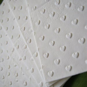 Puede incluir: Un paquete de servilletas de papel blancas con un sutil patr&oacute;n de corazones en relieve. Las servilletas est&aacute;n dobladas en forma de abanico.