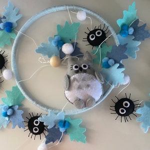 May include: A handmade mobile featuring a light blue ring adorned with felt leaves in shades of blue and white pom-poms. A gray Totoro figure and black soot sprites are attached, creating a whimsical nursery decoration.