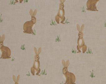 May include: A repeating pattern of brown rabbits and green grass sprigs on a beige background. The rabbits are in various poses, some sitting and some standing, with long ears and fluffy tails. The fabric has a linen-like texture.