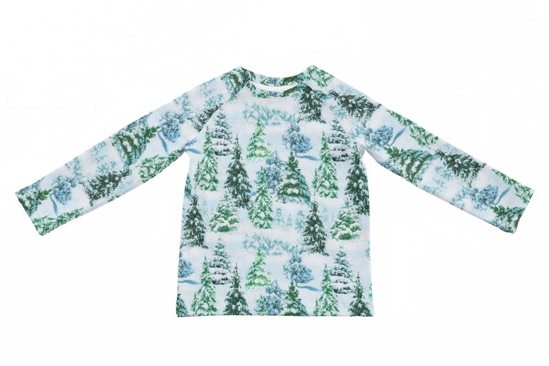 以下が含まれることがあります： 白い背景に、雪で覆われた緑と青の木が繰り返し描かれた長袖シャツです。