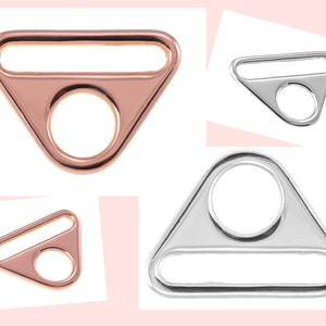 Könnte beinhalten: Zwei dreieckige Metallringe mit einer flachen Leiste oben und einem runden Loch in der Mitte. Ein Ring ist roségoldfarben und der andere silberfarben.