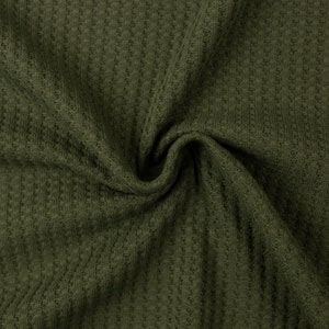 Può includere: Primo piano di un tessuto a maglia waffle verde. Il tessuto è morbido e testurizzato, con un sottile motivo a waffle.