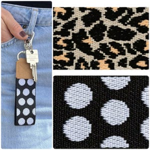 Op de afbeelding: Een zwart-witte polkadot sleutelhanger met een zilveren sluiting en een sleutel. De sleutelhanger is bevestigd aan een spijkerbroek. De afbeelding toont ook close-ups van luipaardprint en polkadot stof.