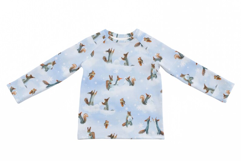 以下が含まれることがあります： 雪の中で遊ぶリスの模様がついた、薄い青色の長袖シャツ。リスは茶色と白で、雪は青みがかった白です。