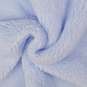 Op de afbeelding: Een close-up van een zachte, lichtblauwe stof met een pluche textuur. De stof is gevouwen en gekreukt, waardoor een zachte en uitnodigende uitstraling ontstaat.