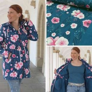Pode incluir: Uma jaqueta azul com capuz com estampa floral que apresenta flores rosa sobre um fundo azul escuro. A jaqueta tem fecho de zíper e cintura com cordão.