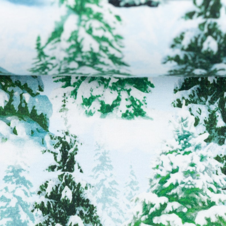以下が含まれることがあります： 白い生地に、白い雪で覆われた緑色の松の木が繰り返しパターンで描かれています。生地は柔らかく、質感があります。