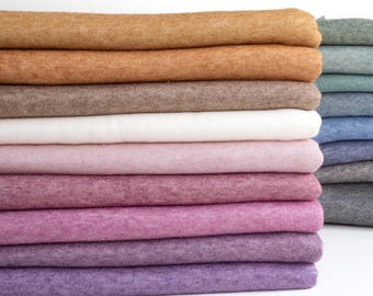 Könnte beinhalten: Ein Stapel gefalteten Stoffes in verschiedenen Brauntönen, Rosa, Lila und Weiß. Der Stoff ist weich und texturiert und scheint eine Art Strickware zu sein.