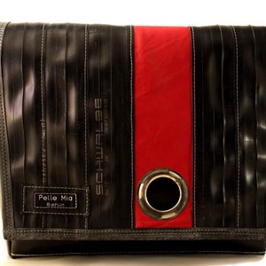 Könnte beinhalten: Eine schwarze Messenger Bag aus recycelten Fahrradschlauch mit rotem Streifen und einem Metallösen. Die Tasche hat einen schwarzen Lederriemen und den Text "Pelle Mia Berlin" und "Schwalbe" auf der Vorderseite.