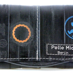 Könnte beinhalten: Schwarze Geldbörse aus recyceltem Reifen-Innenschlauch mit orangefarbenen und blauen Kreisdesigns. Die Geldbörse hat weiße Nähte und ein schwarzes Etikett mit der Aufschrift "Pelle Mia Berlin".