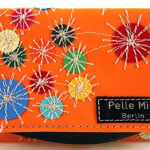 Könnte beinhalten: Orangefarbenes Lederportemonnaie mit bunten Kreisen und weißen Nähten. Das Portemonnaie hat ein schwarzes Etikett mit dem Text "Pelle Mia Berlin".