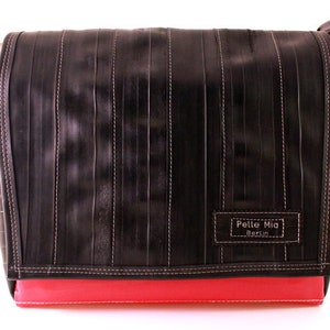 Könnte beinhalten: Eine schwarze Umhängetasche aus recycelten Reifeninnenschläuchen. Die Tasche hat einen roten Boden und einen weißen Patch mit dem Text "Pelle Mia Berlin".