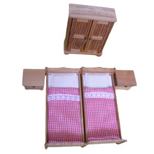 Op de afbeelding: Een poppenhuis slaapkamerset met twee eenpersoonsbedden, twee nachtkastjes en een houten kledingkast. De bedden hebben roze en wit geruite beddengoed en witte kussens. De nachtkastjes en de kledingkast zijn gemaakt van onbehandeld hout.