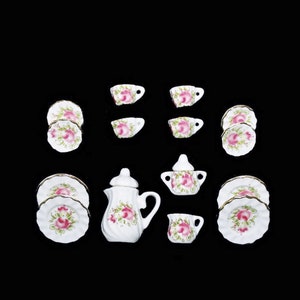 May include: A miniature tea set with a white teapot, sugar bowl, creamer, and four cups and saucers. The set features a floral design with pink roses and green leaves.