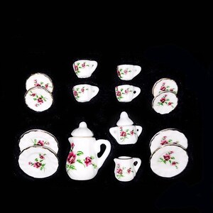 May include: A miniature tea set with a white background and pink rose pattern. The set includes a teapot, creamer, sugar bowl, four cups, and four saucers.