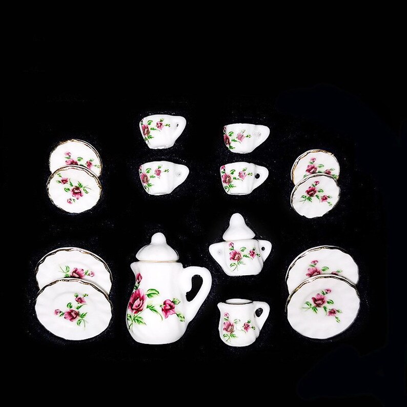 May include: A miniature tea set with a white background and pink rose pattern. The set includes a teapot, creamer, sugar bowl, four cups, and four saucers.