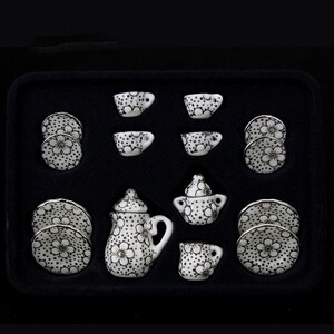 May include: A white porcelain tea set with black and gold floral designs. The set includes a teapot, creamer, sugar bowl, four cups, and four saucers. The set is packaged in a black box with a white interior.