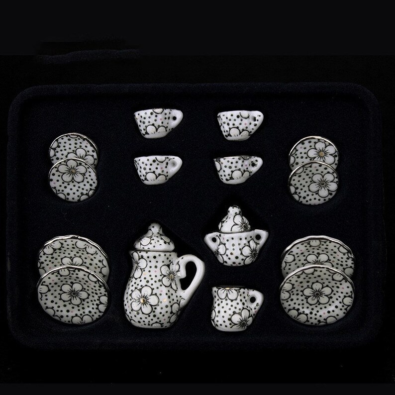 May include: A white porcelain tea set with black and gold floral designs. The set includes a teapot, creamer, sugar bowl, four cups, and four saucers. The set is packaged in a black box with a white interior.