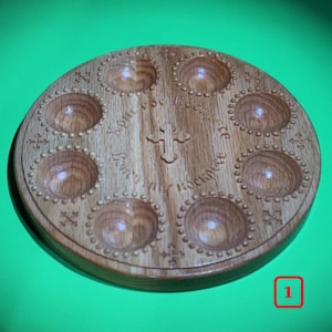 May include: A wooden egg tray with seven individual compartments, each with a decorative border of small circles. The tray is inscribed with the words "In my Father's house are many mansions" and a cross.