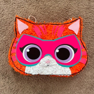 May include: Orange and pink cat piñata with a superhero mask and large eyes.