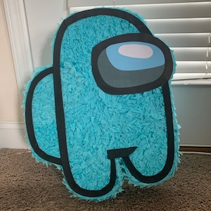 May include: A light blue Among Us piñata. The piñata is shaped like the game character with a light blue body, black outline, and a gray and white visor. The piñata is made of blue crepe paper.