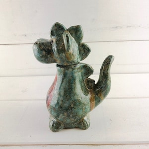 Könnte beinhalten: Eine Keramik-Drachenfigur mit grüner und brauner Glasur. Der Drache hat einen stacheligen Rücken und einen langen Schwanz.