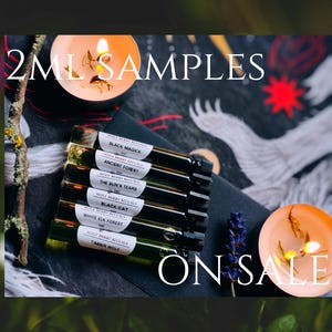 Puede incluir: Imagen que presenta varios pequeños viales de vidrio etiquetados con nombres como "Black Magick" y "Ancient Forest". Los viales están dispuestos sobre una superficie oscura, acompañados de velas encendidas y el texto "2ML SAMPLES" y "ON SALE".
