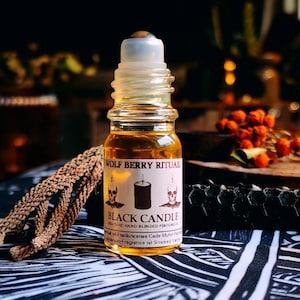 Pode incluir: Um pequeno frasco de perfume de vidro com um aplicador roll-on. O frasco é preenchido com um líquido dourado e tem um rótulo que diz "WOLF BERRY RITUALS BLACK CANDLE". O rótulo apresenta ilustrações de caveiras e uma vela.