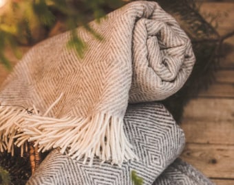 May include: A gray and white diamond patterned throw blanket with fringe. The blanket is folded and rolled up, and is sitting on a wooden surface.