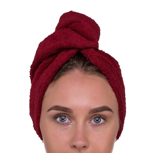 Op de afbeelding: Een vrouw met een bordeauxrode handdoek om haar hoofd. De handdoek is bovenop haar hoofd in een knoop geknoopt.